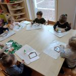 Dzieci siedzą przy stoliku i wykonują pracę plastyczną z kolorowego papieru
