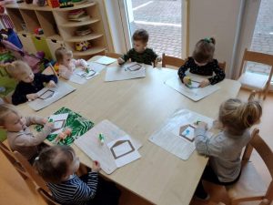 Dzieci siedzą przy stoliku i wykonują pracę plastyczną z kolorowego papieru