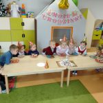 Dzieci siedząc przy stoliku nachylają się nad tortem z babeczek