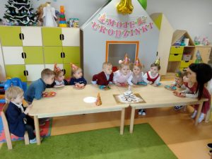 Dzieci siedząc przy stoliku nachylają się nad tortem z babeczek