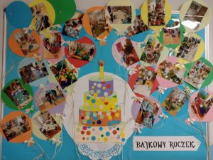 Gazetka ścienna przedstawiająca tort z papieru kolorowego, wokół tortu zdjęcia dzieci podczas zabaw i zajęć w żłobku