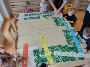 Dzieci siedzą przy stoliku i robią pracę plastyczną z papieru: zimowy szalik