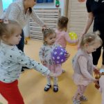Dzieci tańczą w kole. Pośrodku dziewczynka z fioletowym balonikiem