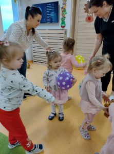 Dzieci tańczą w kole. Pośrodku dziewczynka z fioletowym balonikiem