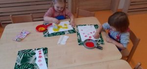Dzieci odbijają kolorowe kształty przy pomocy stempli na białych kartkach papieru