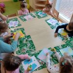 Dzieci przy stoliku robią pracę plastyczną z papieru: rękawiczki