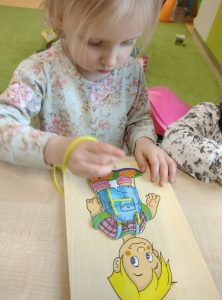Dziewczynka przewleka sznurowadło przez otwory w drewnianej deseczce z rysunkiem chłopca