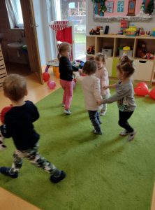 Dzieci trzymają się za ręce i tańczą w kółeczku.