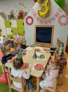 Dzieci siedzą przy stole i częstują się urodzinowymi babeczkami