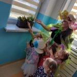 Dzieci wraz z Panią Wiosną podziwiają na oknie w szatni kolorowe kwiatuszki posadzone w doniczce przez dzieci na zajęciach.