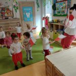 Dzieci tańczą wraz z opiekunką ubrane na biało- czerwono. W dłoniach trzymają chorągiewki biało- czerwone wymachując nimi.