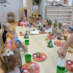 Dzieci siedzą przy stoliku i częstują się urodzinowymi muffinkami. Na głowie mają ubrane urodzinowe czapeczki.