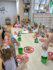Dzieci siedzą przy stoliku i częstują się urodzinowymi muffinkami. Na głowie mają ubrane urodzinowe czapeczki.