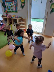 Dzieci tańczą z kolorowymi balonikami do ulubionych piosenek. W tle widać sale zabaw.