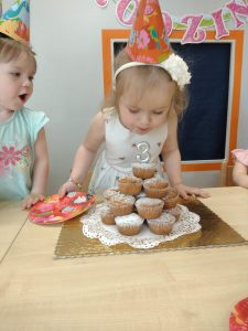 Solenizantka dmucha świeczkę w kształcie cyfry 3 wbitą w torcik muffinkowy.