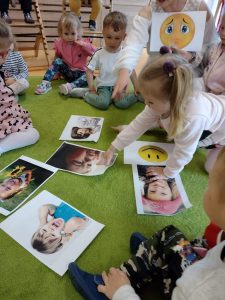 Dzieci oglądają rozłożone na dywanie fotografię związane z emocjami.