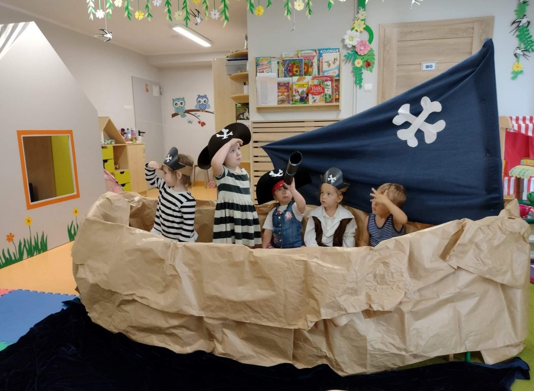 Dzieci ubrane w stroje piratów siedzą w statku zrobionym z szarego papieru.