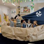 Dzieci ubrane w stroje piratów siedzą w statku zrobionym z szarego papieru.