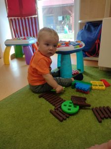Chłopczyk siedzi na zielonym dywanie i bawi się stolikiem interaktywnym.