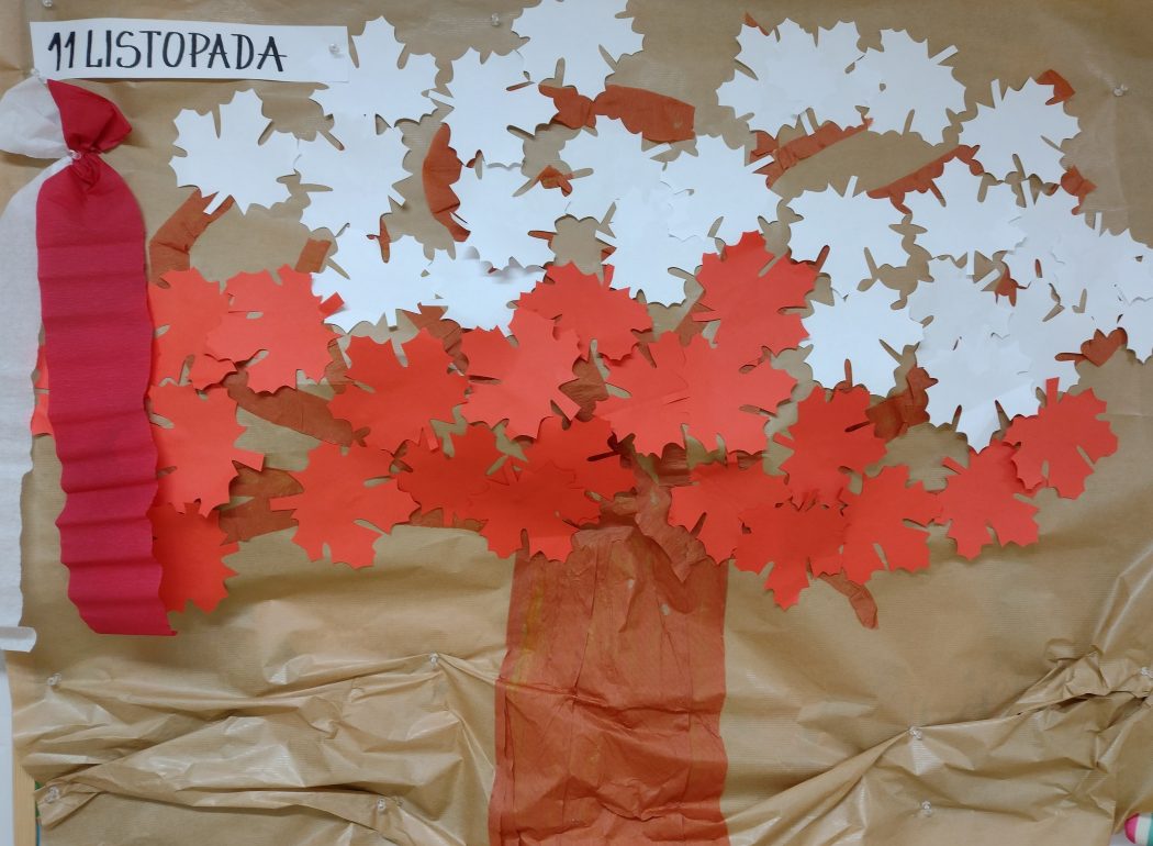 Zdjęcie przedstawia drzewo udekorowane biało-czerwonymi liśćmi klonu.