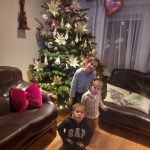 Dwoje chłopców z dziewczynką pozują do zdjęcia na tle świątecznej choinki.