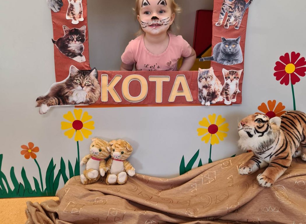 Dziewczynka stoi i pozuje do zdjęcia w ramce z napisem "Dzień Kota".