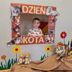 Chłopiec stoi i pozuje do zdjęcia w ramce z napisem "Dzień Kota".