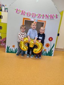 Trzech chłopców stoi trzymając duży złoty balon w kształcie cyfry trzy.