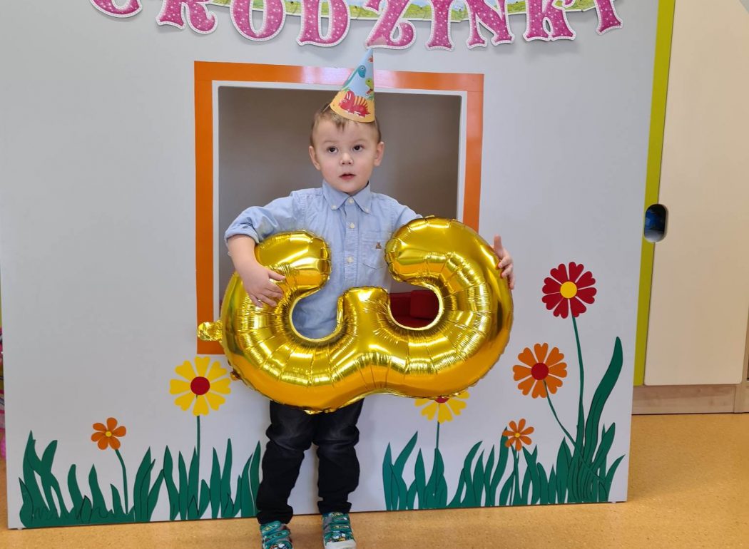 Chłopiec stoi trzymając w rękach duży złoty balon w kształcie trzy.