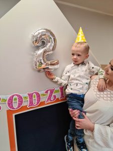 Opiekunka trzyma chłopca na rękach przy dekoracji urodzinowej.