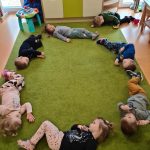 Dzieci leżą na dywanie tworząc duże koło.