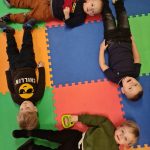 Dzieci leżą na dywanie tworząc kwadrat.
