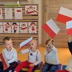 Dzieci siedzą na podusiach i do piosenki o Polsce machają flagami.