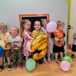 Dzieci stoją koło siebie pozując do zdjęcia, trzymając kolorowe baloniki.