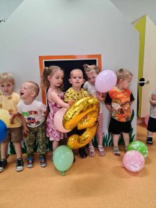 Dzieci stoją koło siebie pozując do zdjęcia, trzymając kolorowe baloniki.