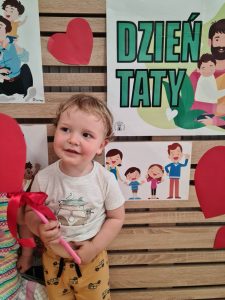 Chłopiec stoi i trzyma dyplom dla Taty. W tle widać zielony napis "Dzień Taty"