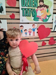 Chłopiec stoi i trzyma dyplom dla Taty. W tle widać zielony napis "Dzień Taty"