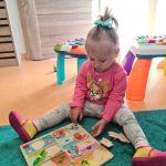 Dziewczynka siedzi na turkusowym dywanie i układa drewniane puzzle.