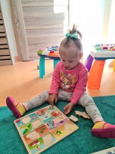 Dziewczynka siedzi na turkusowym dywanie i układa drewniane puzzle.