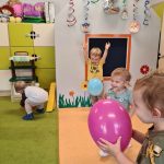 Dzieci bawią się kolorowymi balonami. W tle sala zabaw ozdobiona urodzinowymi dekoracjami.