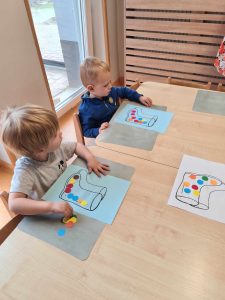 Dwóch chłopców siedzi przy stole i przykleja kolorowe kółeczka na narysowane na kartce papieru kalosze.