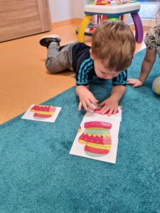 Chłopiec leży na turkusowym dywanie i układa puzzle przedstawiające kolorowe rękawiczki.