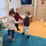 Dzieci trzymają się za ręce i tańczą w kółku na turkusowym dywanie