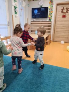Dzieci trzymają się za ręce i tańczą w kółku na turkusowym dywanie