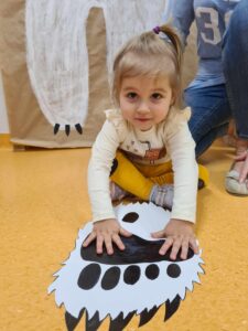 Dziewczynka siedzi na podłodze i trzyma dłonie na wykonanej z papieru łapie niedźwiedzia polarnego.