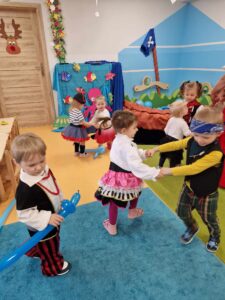 Dzieci ubrane w stroje piratów tańczą na sali zabaw. W tle widać morskie dekoracje.