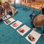 Dzieci siedzą na dywanie i oglądają obrazki przedstawiające psy i ich budy.