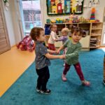 Dzieci tańczą w parach na turkusowym dywanie. W tle widać salę zabaw.