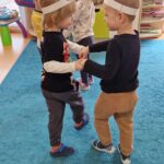 Dzieci mają na głowach kolorowe opaski i tańczą w parach na turkusowym dywanie.