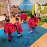 Dzieci przebrane za biedronki tańczą w parach na turkusowym dywanie. W tle widać salę zabaw.